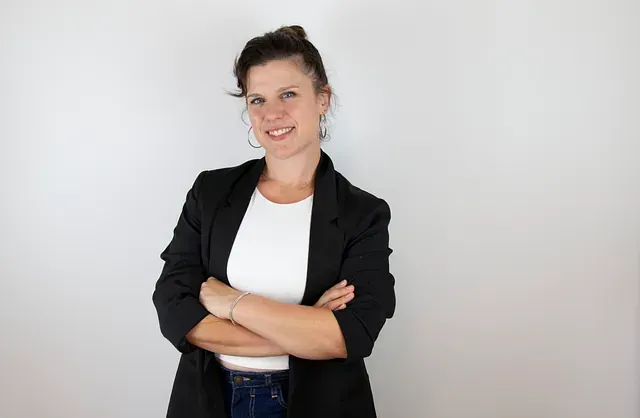 Mujer con blazer negro, con los brazos cruzados, sonriendo a la cámara. Fondo blanco.