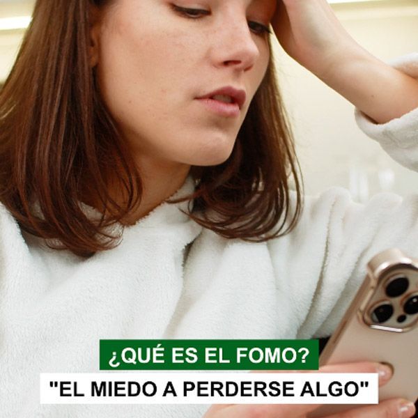 Woman in white sweater looking at phone, with text: “¿QUÉ ES EL FOMO? ‘EL MIEDO A PERDERSE ALGO’”