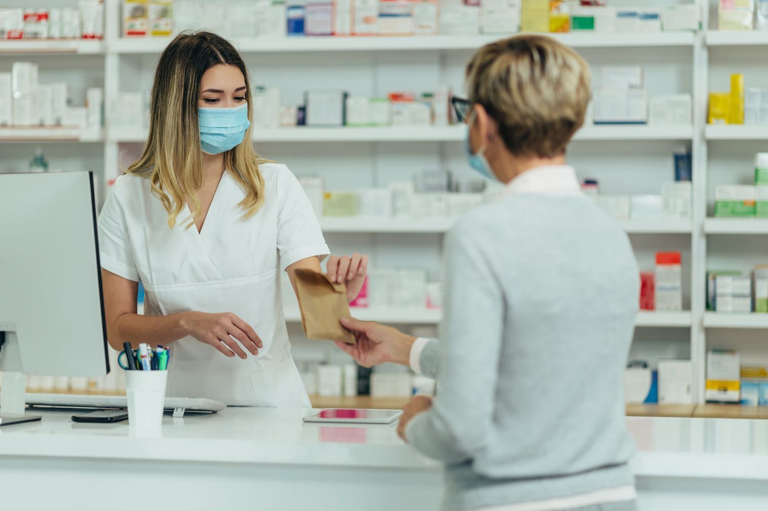 Una mujer que lleva una mascarilla está dando una receta a un farmacéutico en una farmacia.