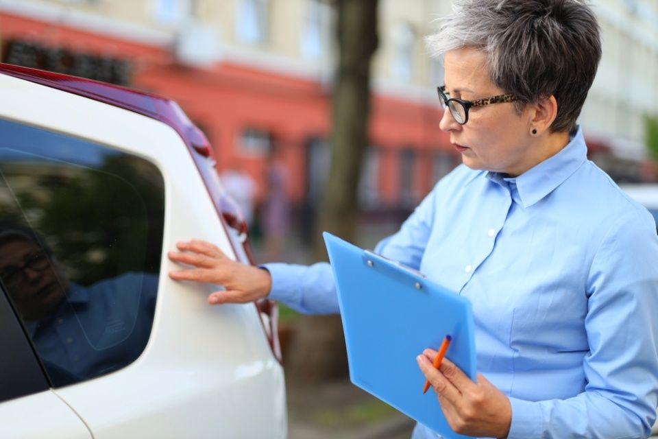 Frau mit Klemmbrett inspiziert Fahrzeug