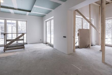 Vista interior de una habitación en construcción con paredes blancas, suelos de hormigón gris claro
