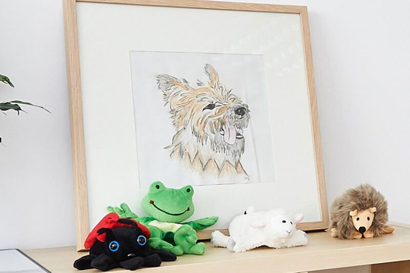 Ein gerahmtes Bild eines Hundes ist von Stofftieren umgeben