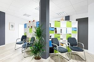Ein Wartezimmer mit Stühlen, einer Pflanze und einem Regal.
