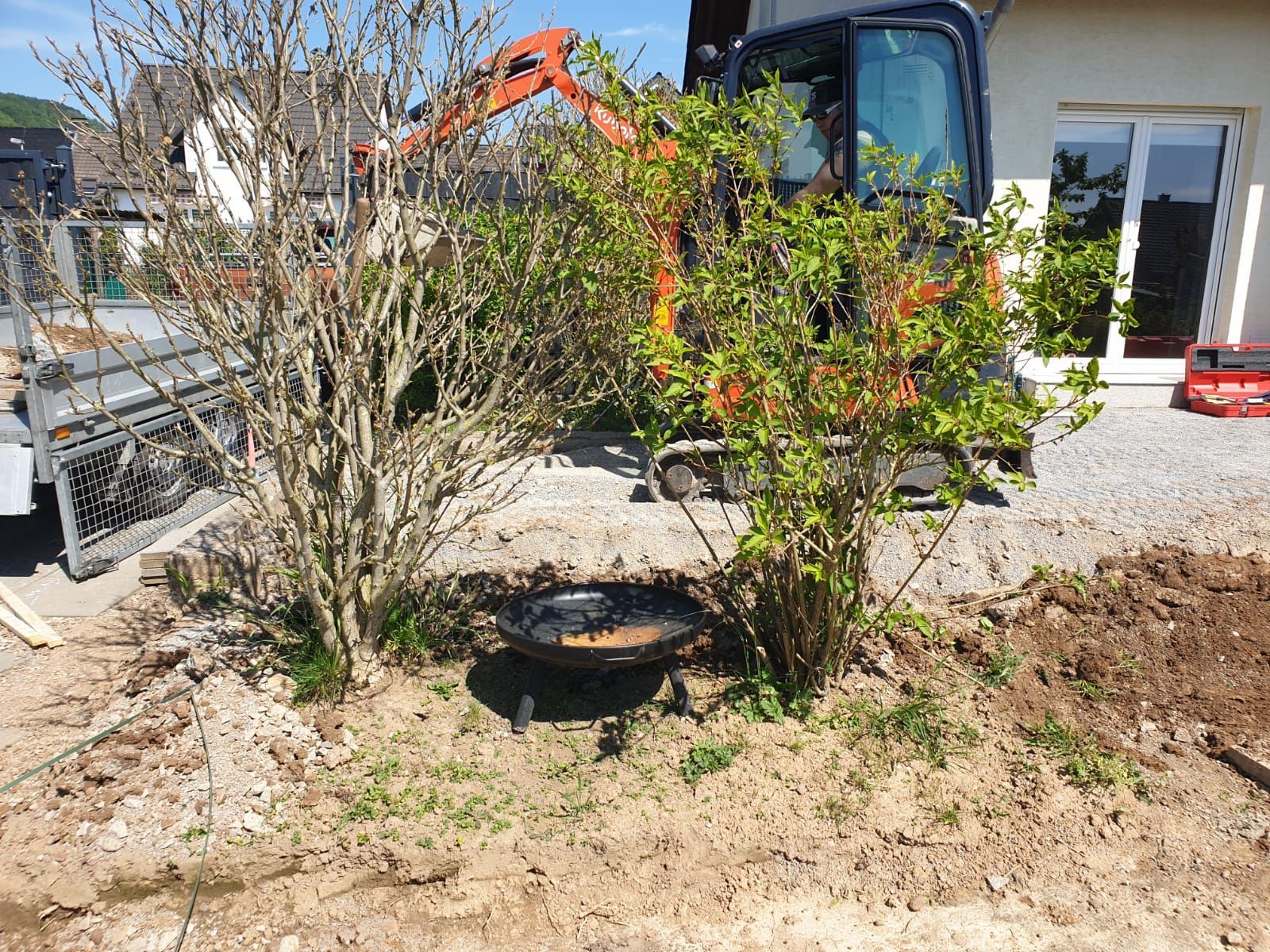 Ein kleiner Bagger gräbt vor einem Haus ein Loch in den Boden.
