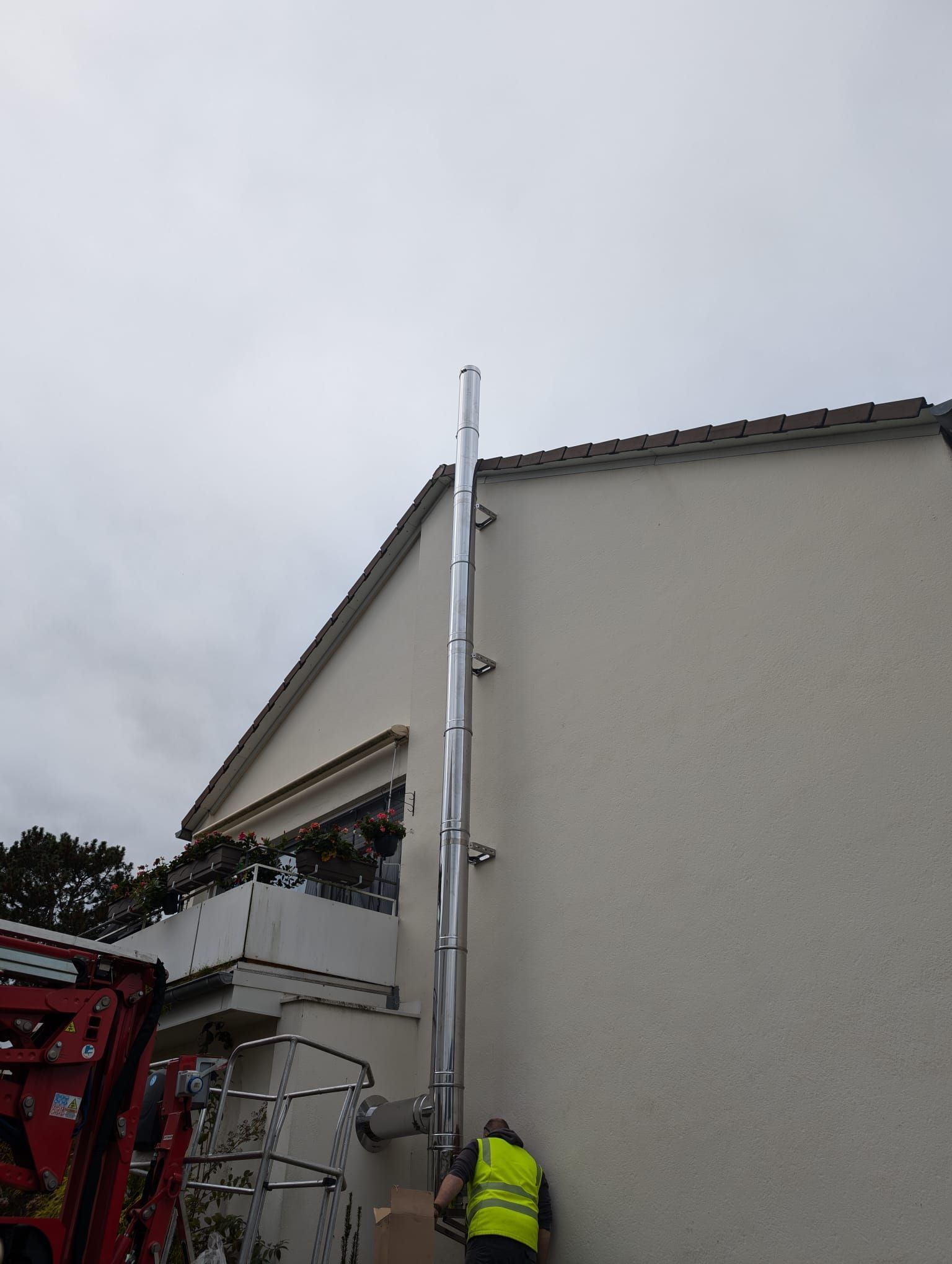 Ein Mann in einer gelben Weste arbeitet an einem Schornstein an der Seite eines Gebäudes.