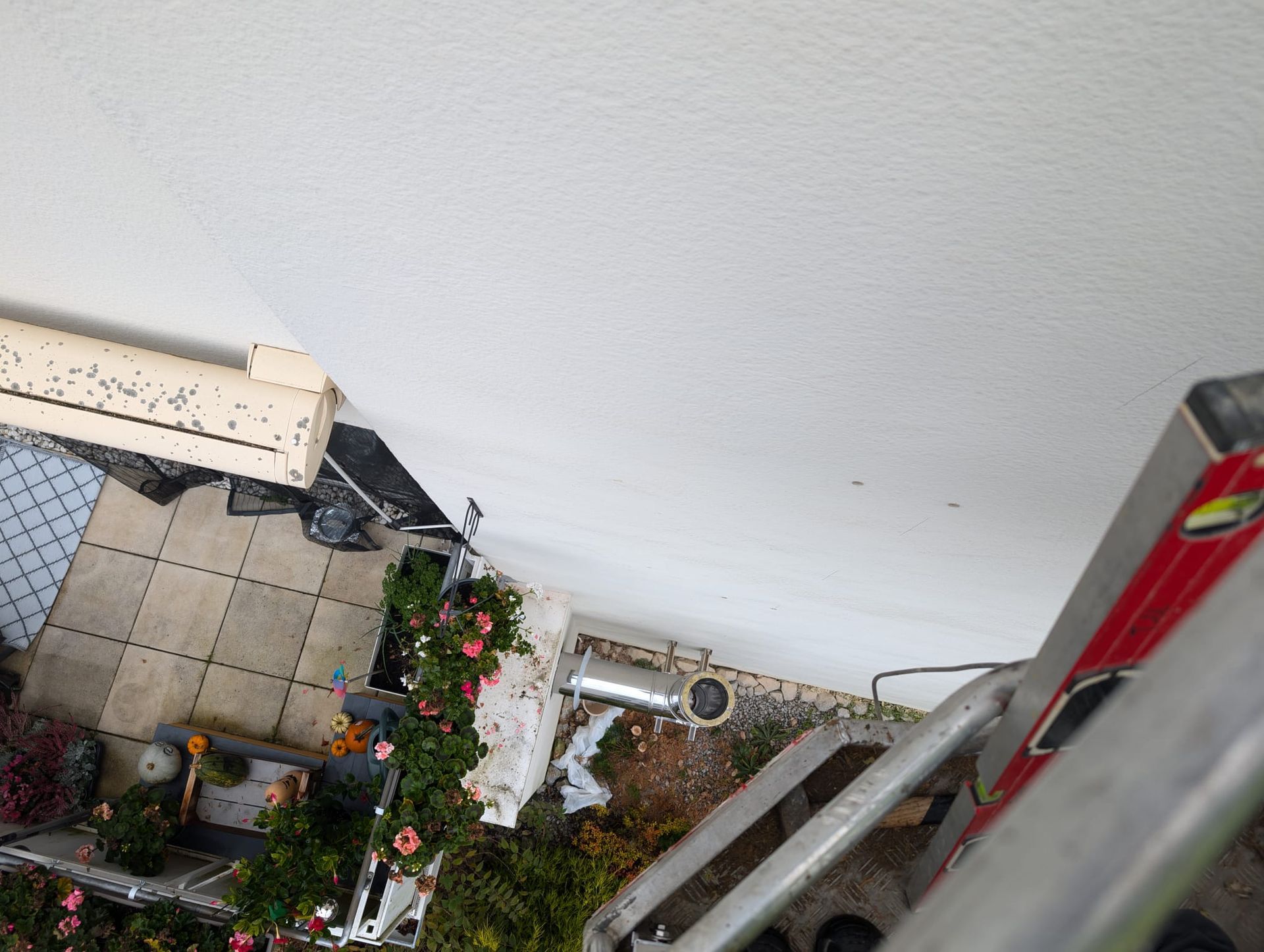 Auf einem Balkon neben einer weißen Wand steht eine Leiter.