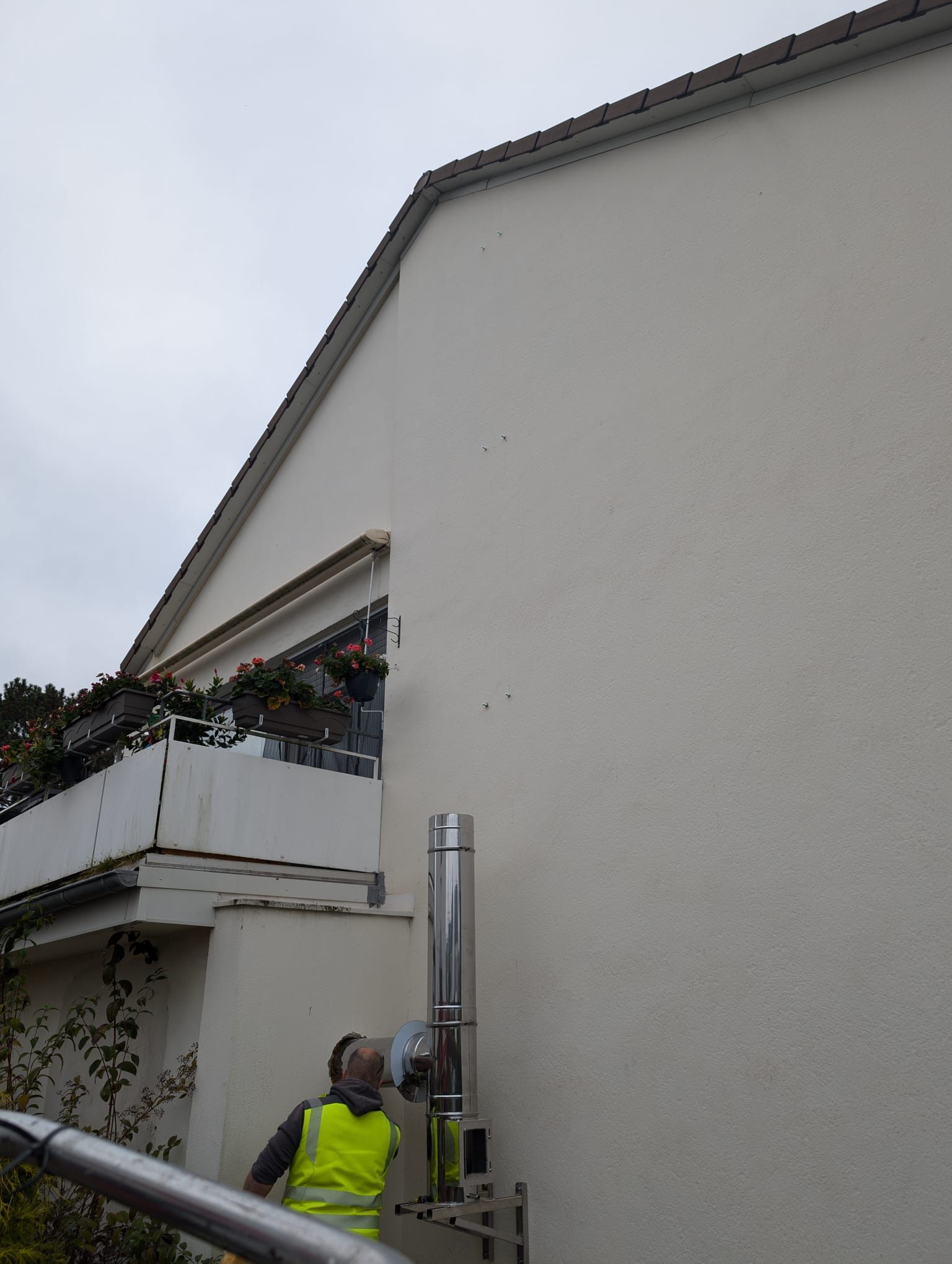 Ein Mann in einer gelben Weste arbeitet an einem Schornstein an der Seite eines Gebäudes.