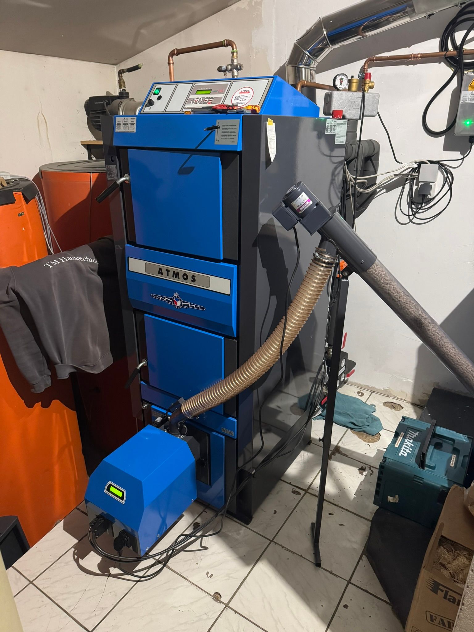 In einem Raum steht auf gefliestem Boden ein blau-schwarzer Heizkessel.