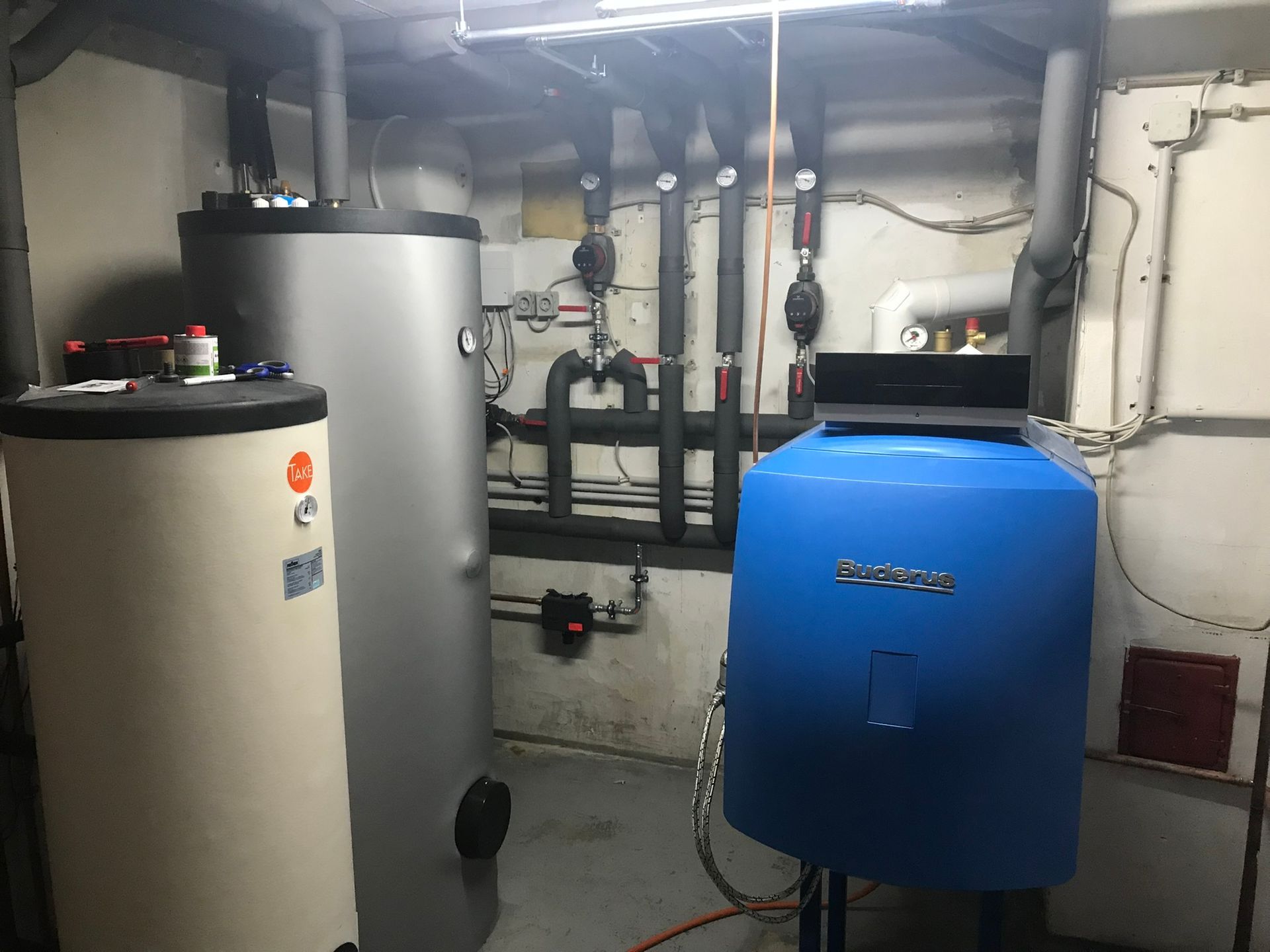 In einem Raum steht ein blauer Heizkessel neben einem weißen Heizkessel.