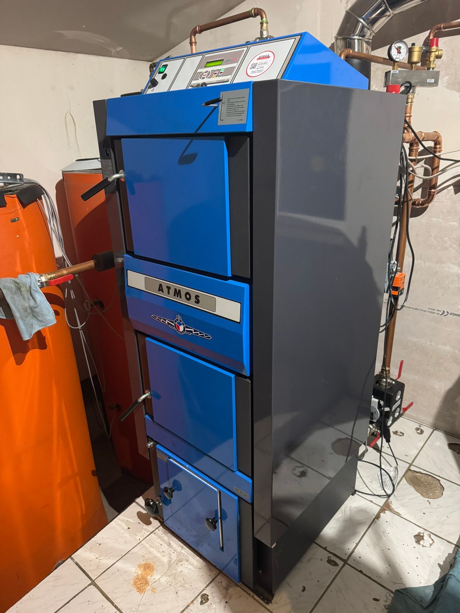 In einem Raum steht auf einem gefliesten Boden ein blau-grauer Heizkessel.