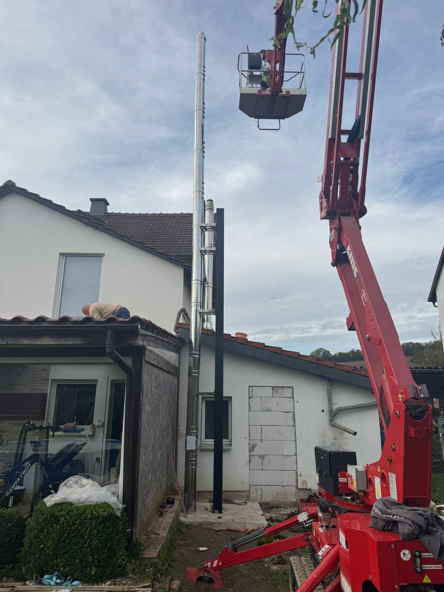 Ein roter Kran arbeitet an einem Schornstein vor einem Haus