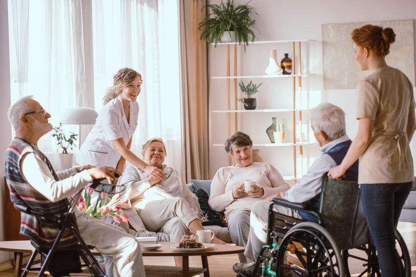 Un grupo de personas mayores están sentadas alrededor de una mesa en una sala de estar.