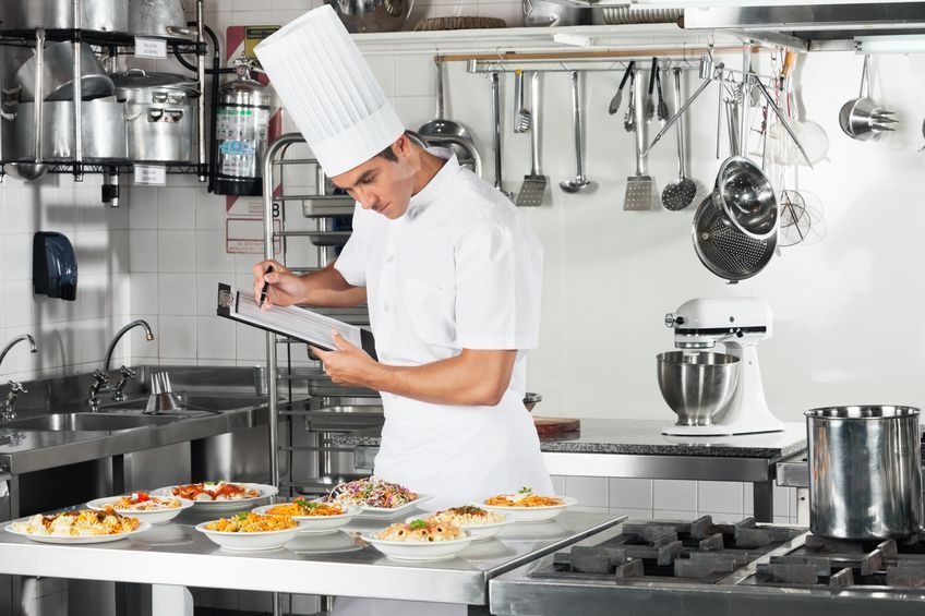 Un chef está escribiendo en un portapapeles en una cocina.