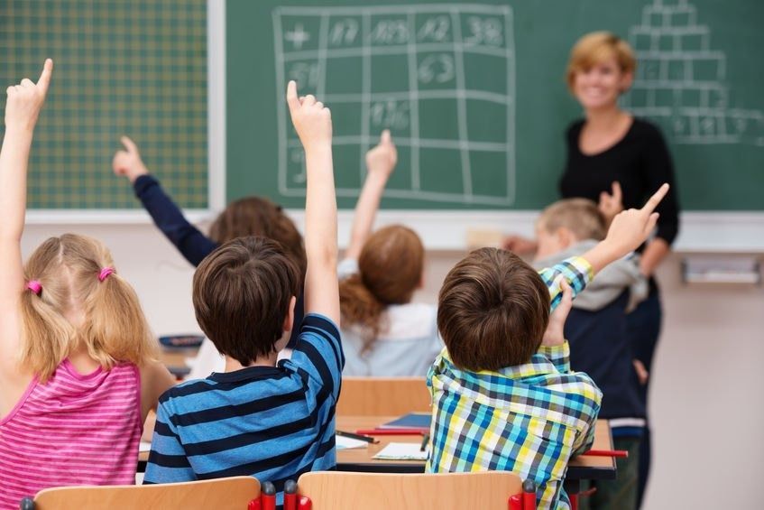 Un grupo de niños levanta la mano en un aula para responder una pregunta.