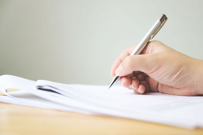 Una persona está escribiendo en un trozo de papel con un bolígrafo.