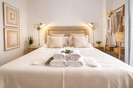 Cama bien hecha con edredón y almohadas beige en un dormitorio luminoso.