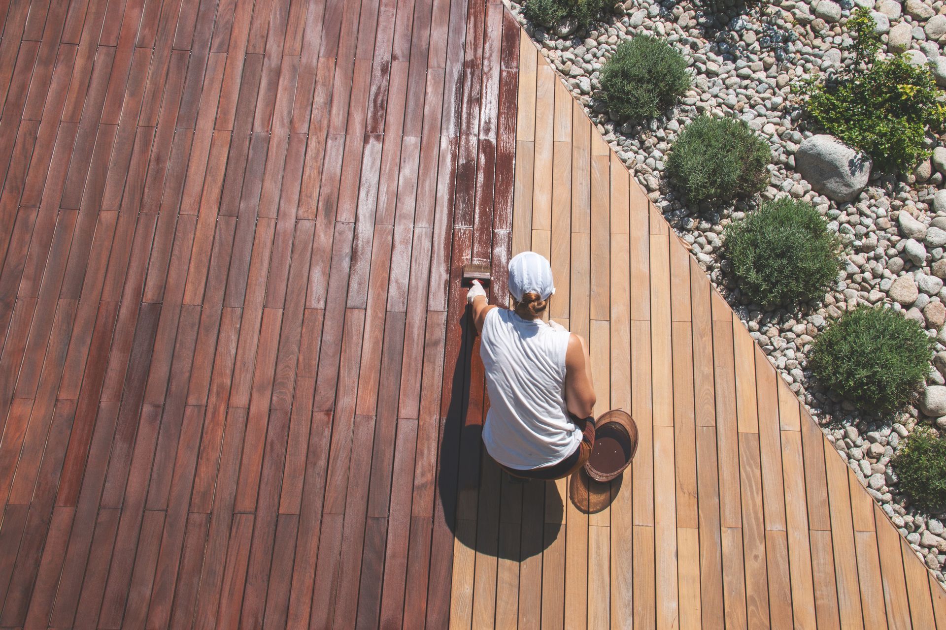 Ein Mann streiche eine Terrasse mit Lasur ein.