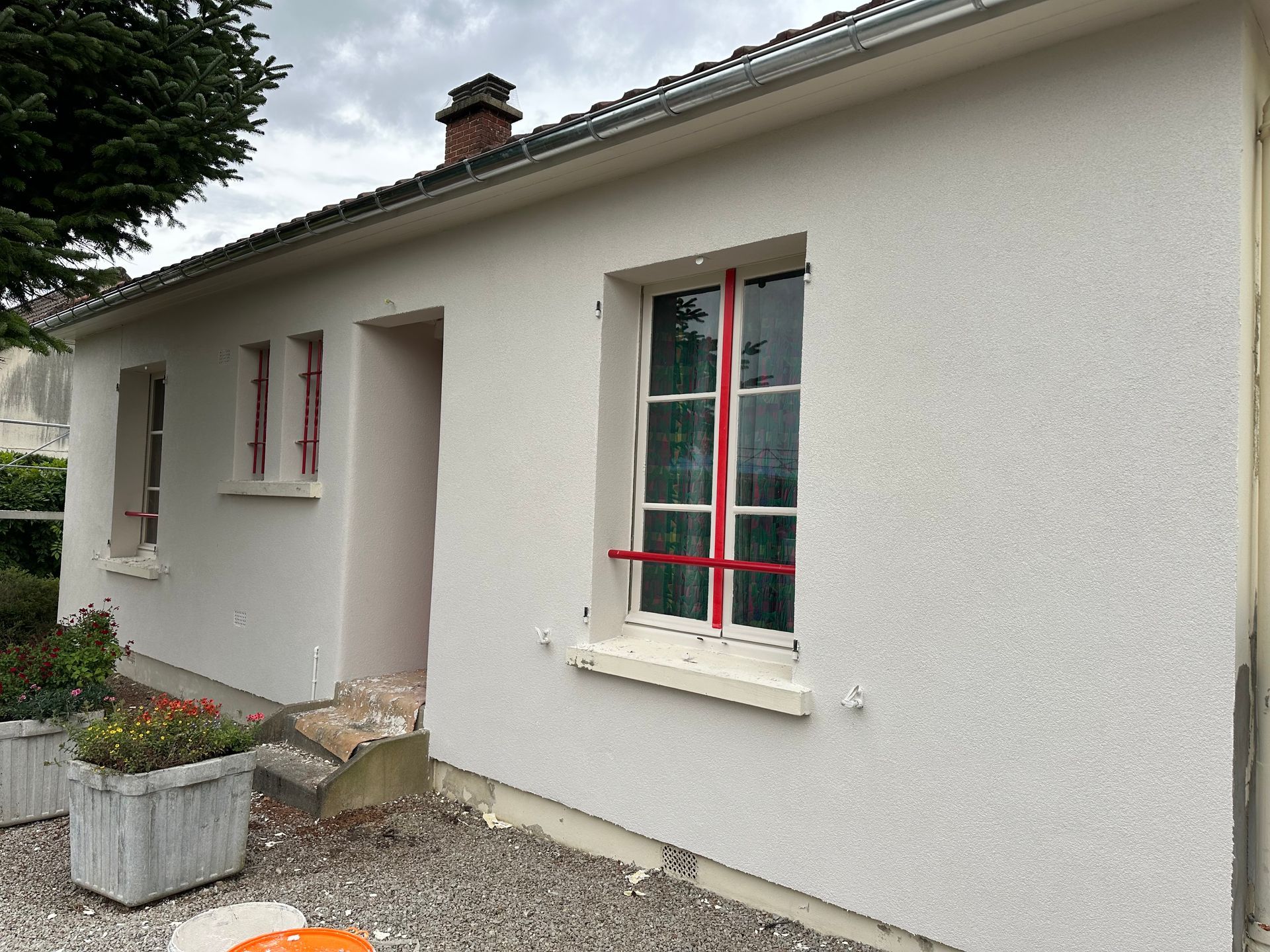 Extérieur d'une maison aux fenêtres encadrées et chemin de graviers à côté d'une jardinière.