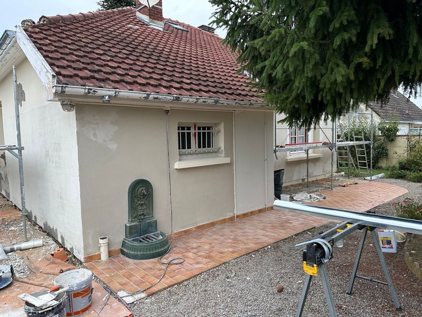 Petite maison au toit de tuiles, une statue en pierre contre le mur et une cour gravillonnée.