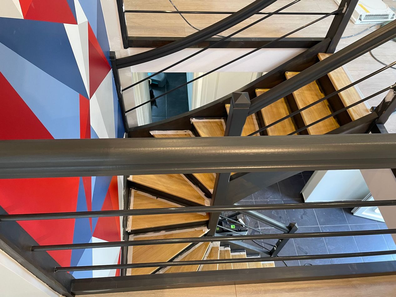 Escalier avec rampes et marches à côté d'une fresque murale géométrique.