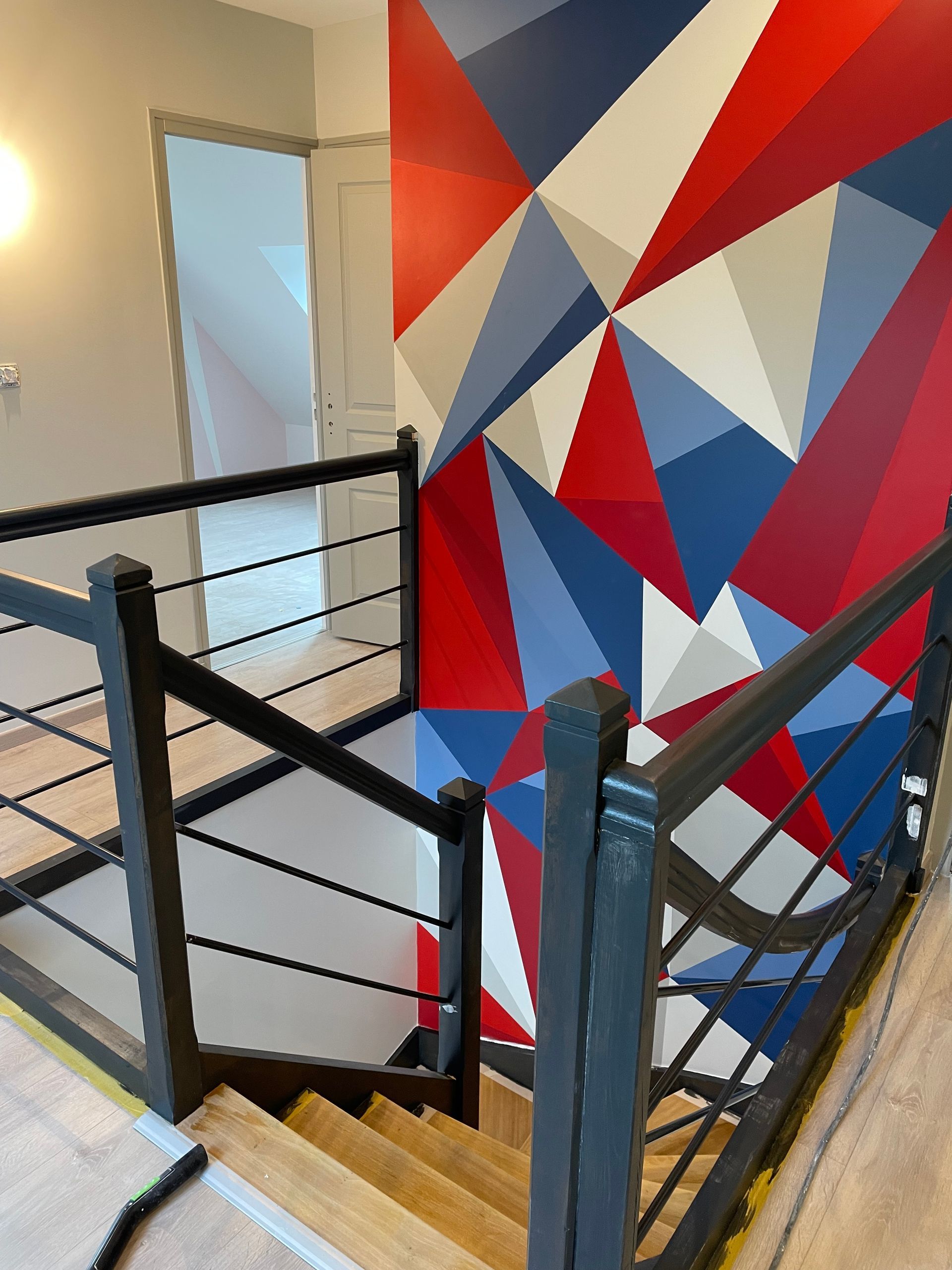 Cage d'escalier avec rampes jouxtant une fresque murale géométrique.