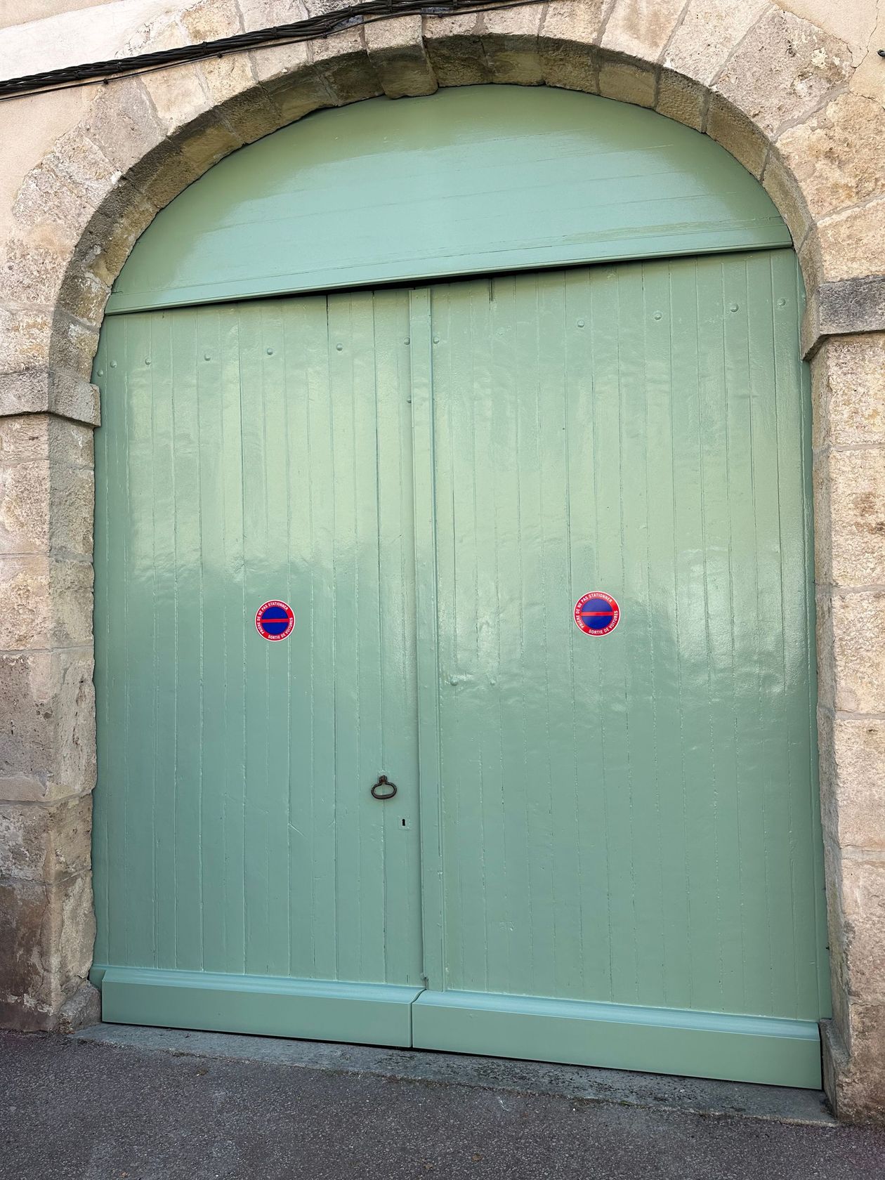 Porte cintrée en bois, encastrée dans un mur de pierre, avec deux petites poignées rondes.