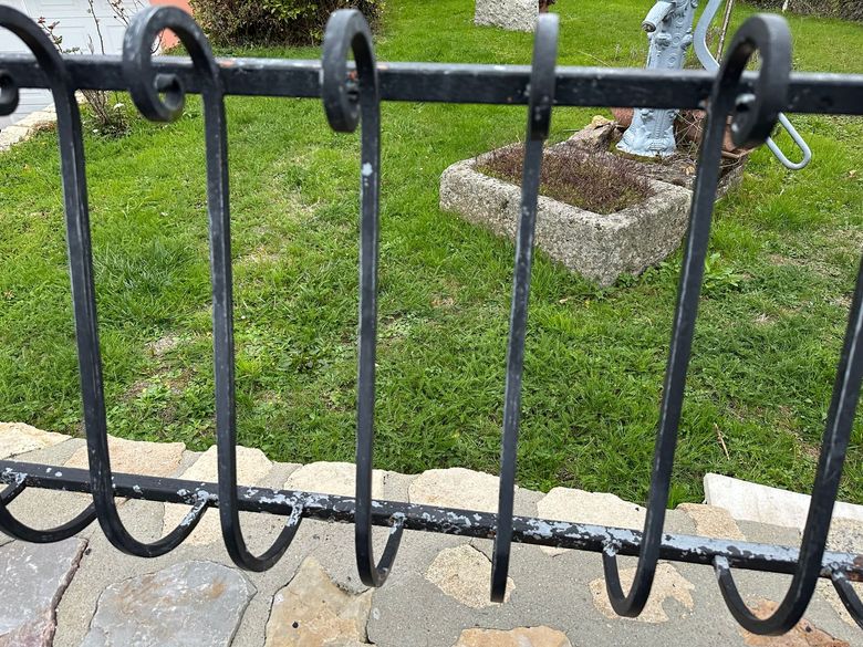Clôture en métal devant une pelouse et une petite jardinière en pierre.