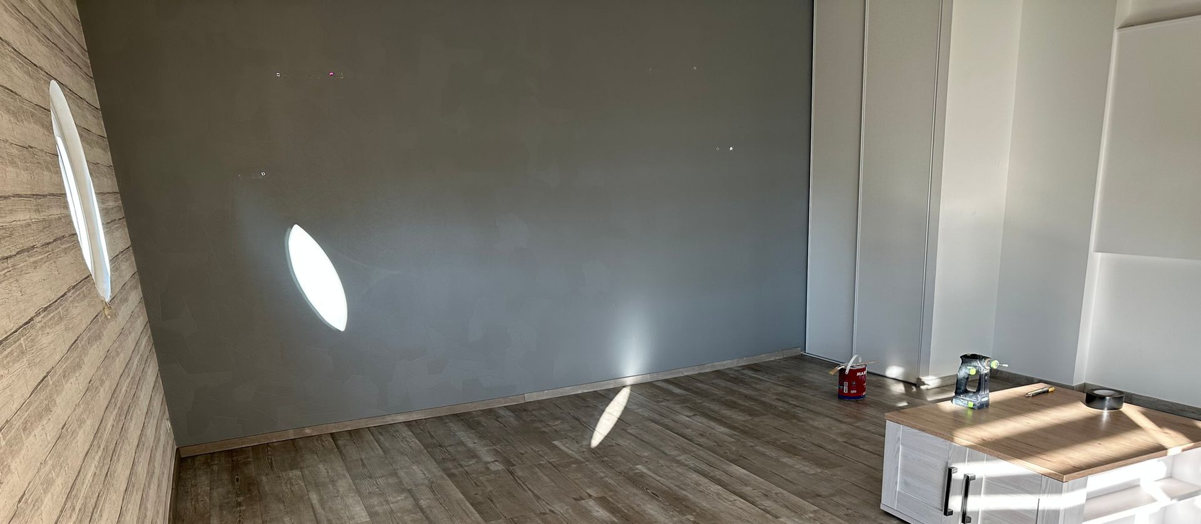 Pièce vide aux murs, au sol en bois et avec une petite table et des objets dans un coin.