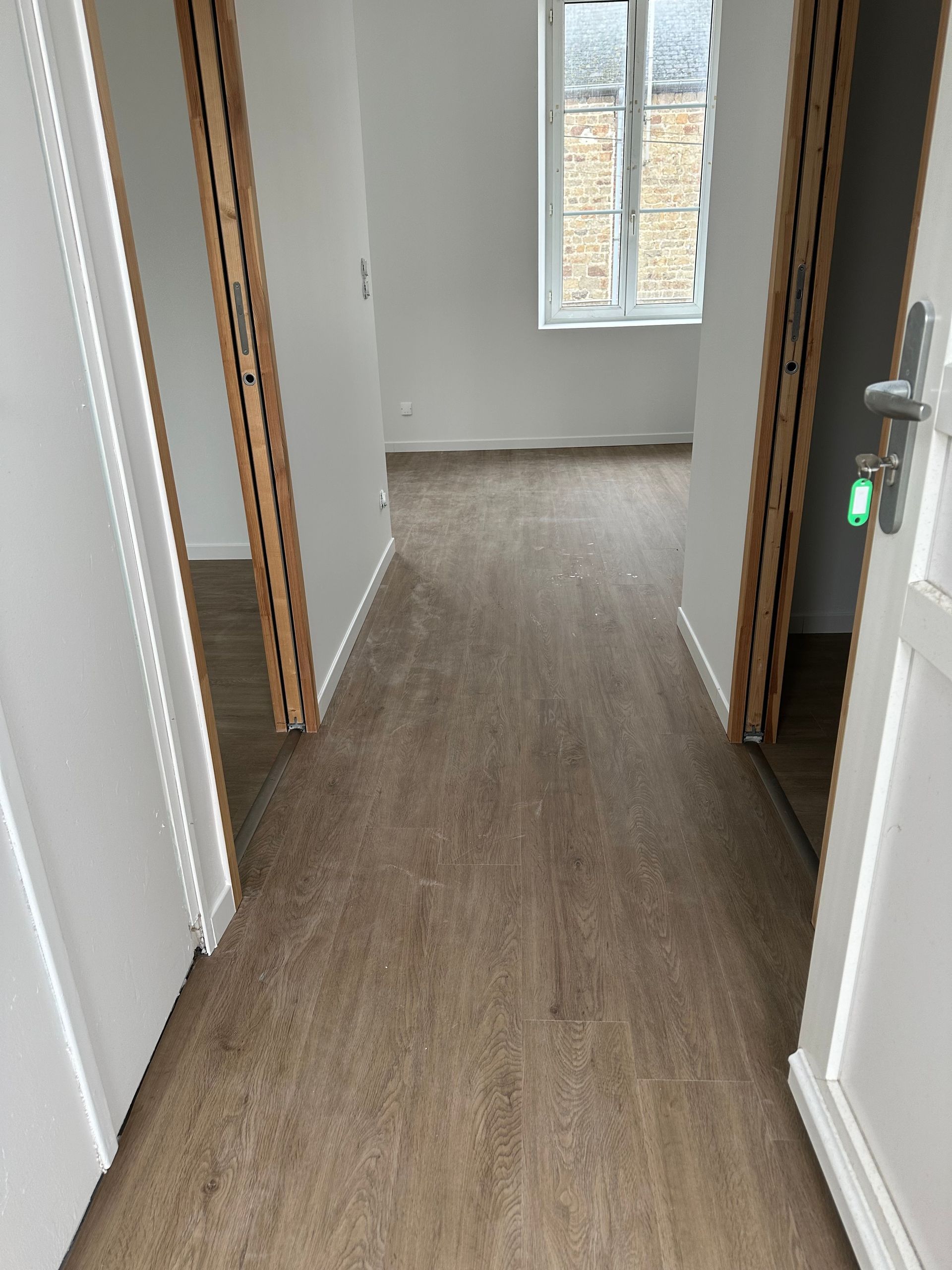 Couloir étroit avec parquet, murs et une fenêtre.