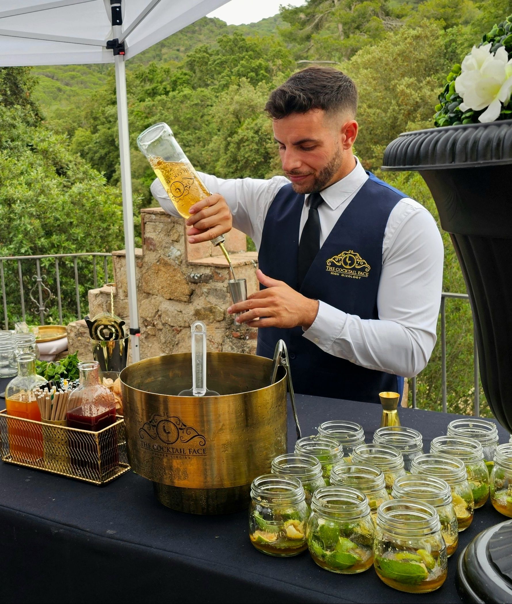 Un camarero vierte un líquido en un vaso medidor. Ambiente al aire libre con cócteles.
