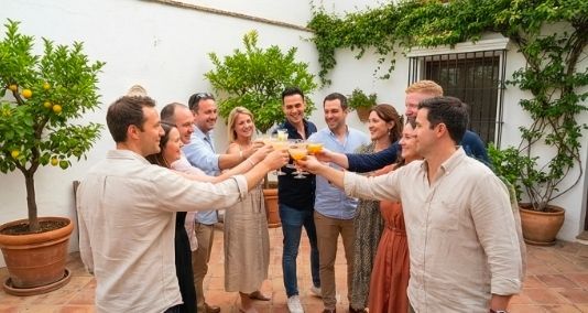 Grupo de personas brindando con bebidas al aire libre, rodeados de plantas, sonriendo.