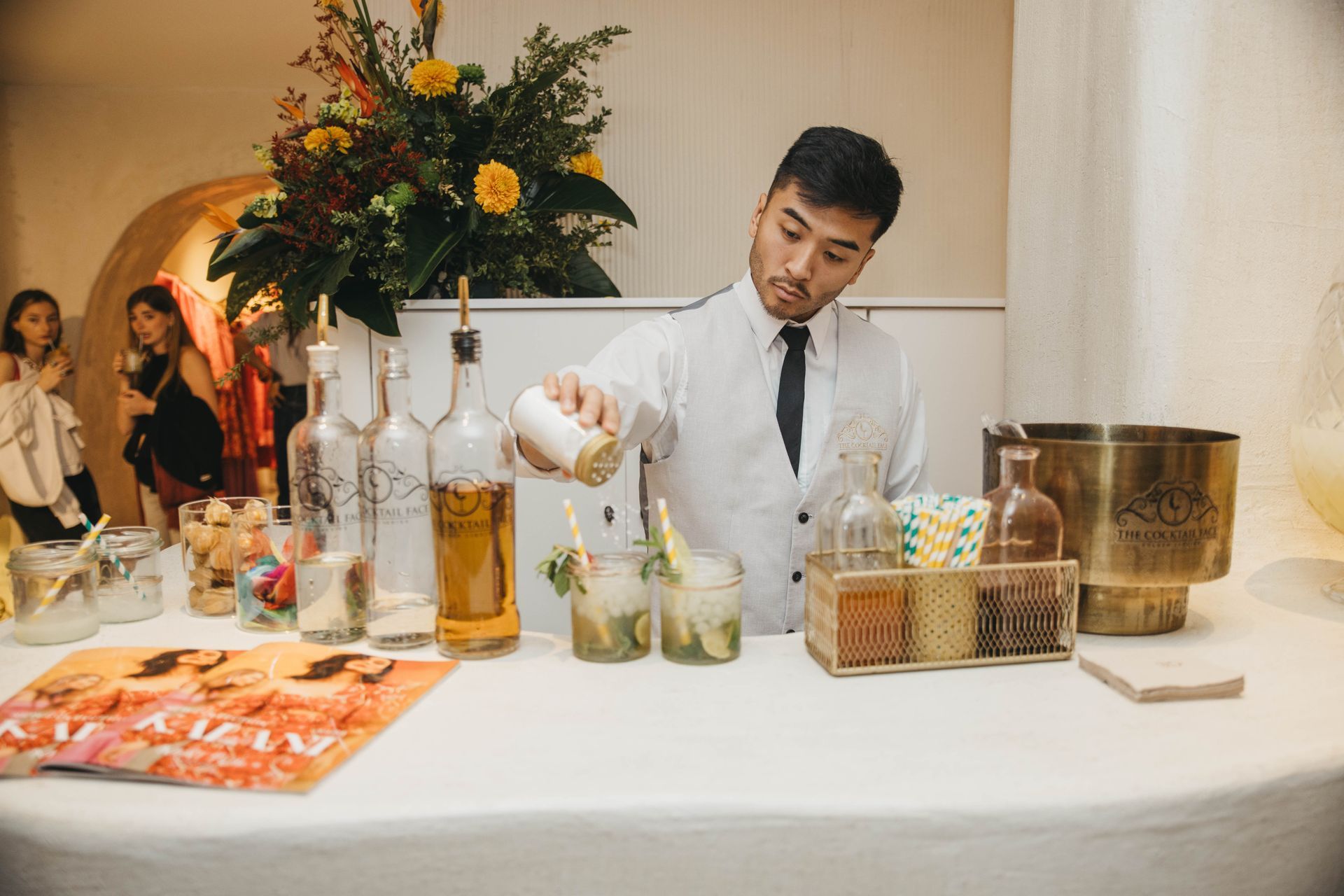 Un camarero sirve líquido en un vaso en un bar. Se exhiben coloridas bebidas e ingredientes.