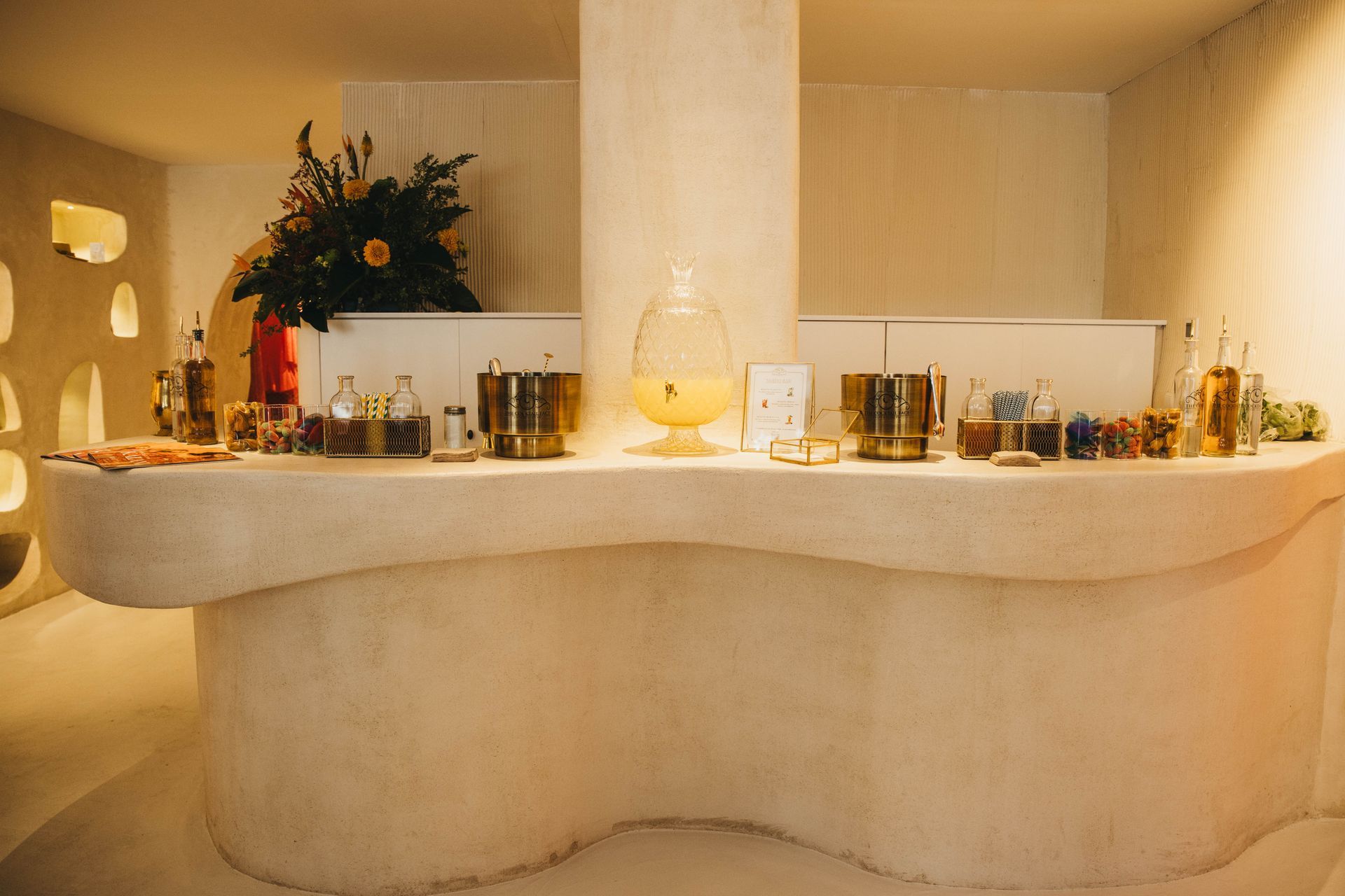 Barra de buffet con bebidas y decoración, en un interior moderno de colores claros.