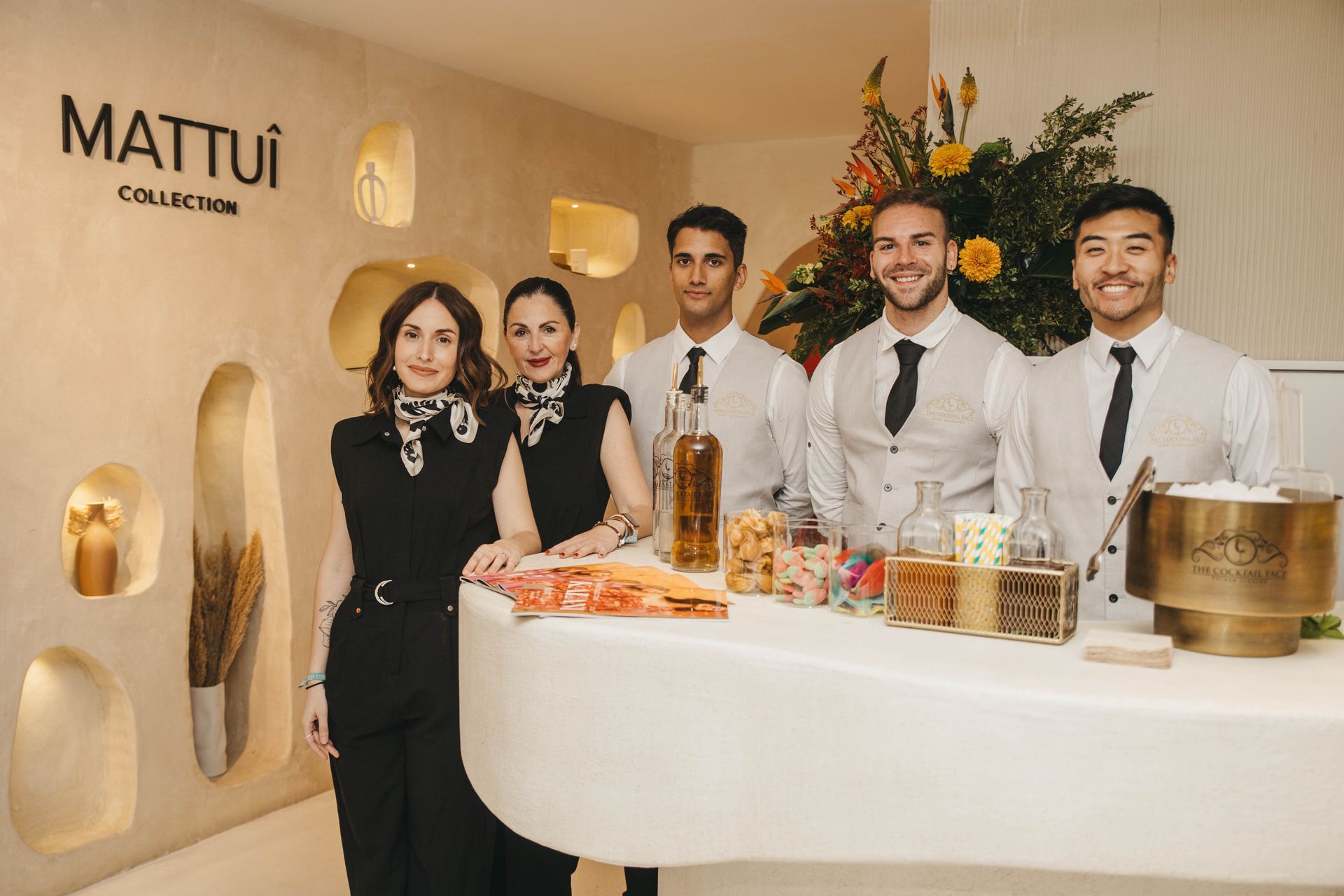 Cinco personas detrás de una barra blanca con dulces. Un cartel de