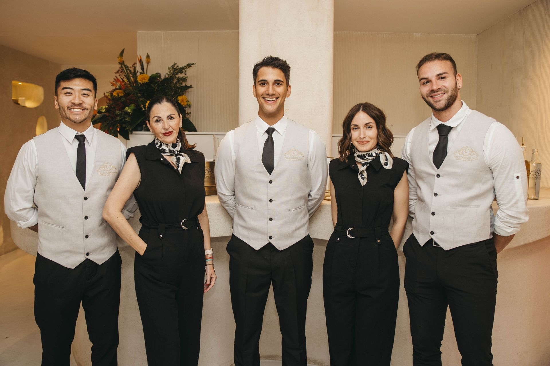 Cinco personas vestidas formalmente están juntas y sonriendo en una habitación bien iluminada.