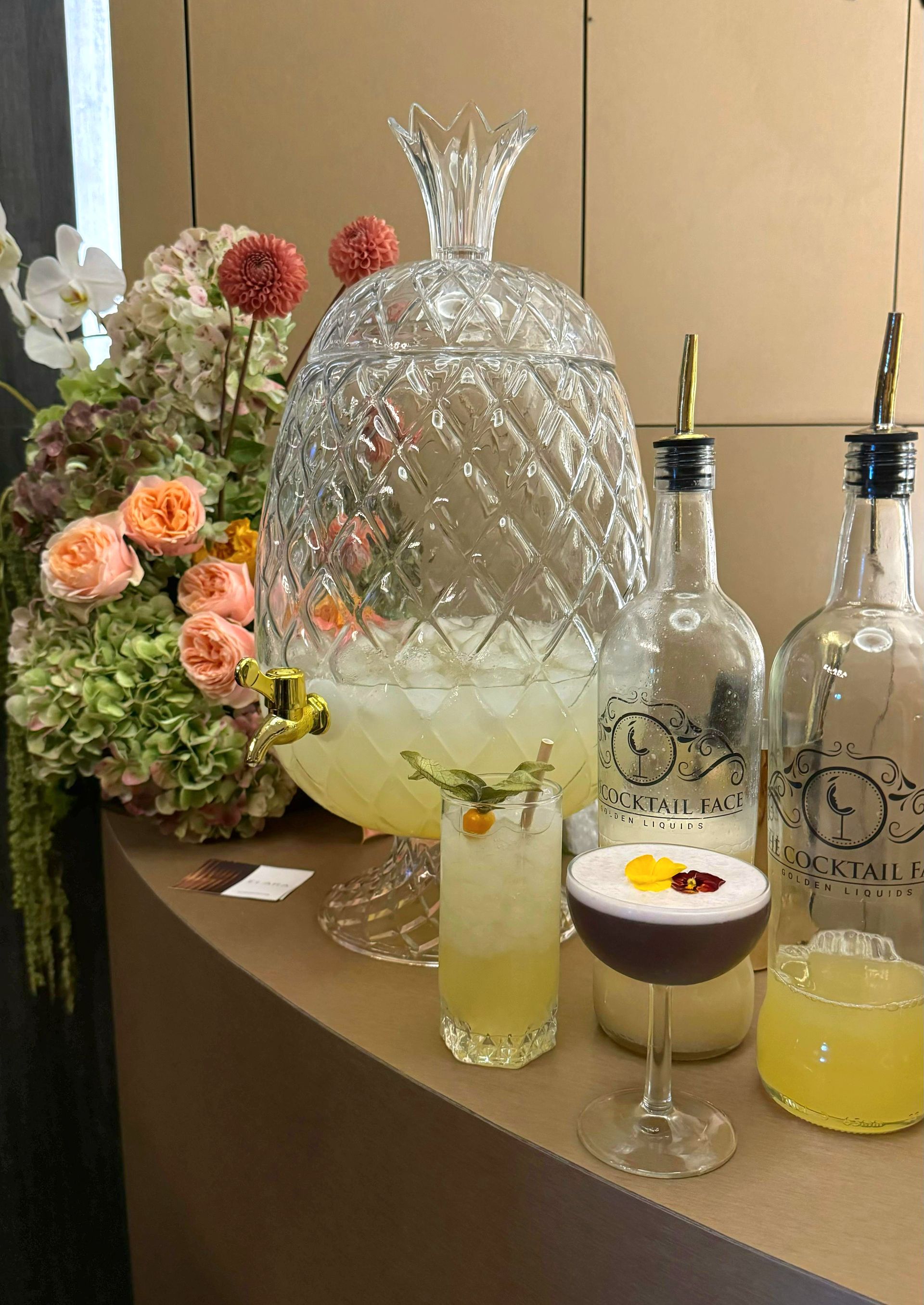 Montaje del bar: ponchera de piña, cócteles, arreglo floral y botellas con vertedor.