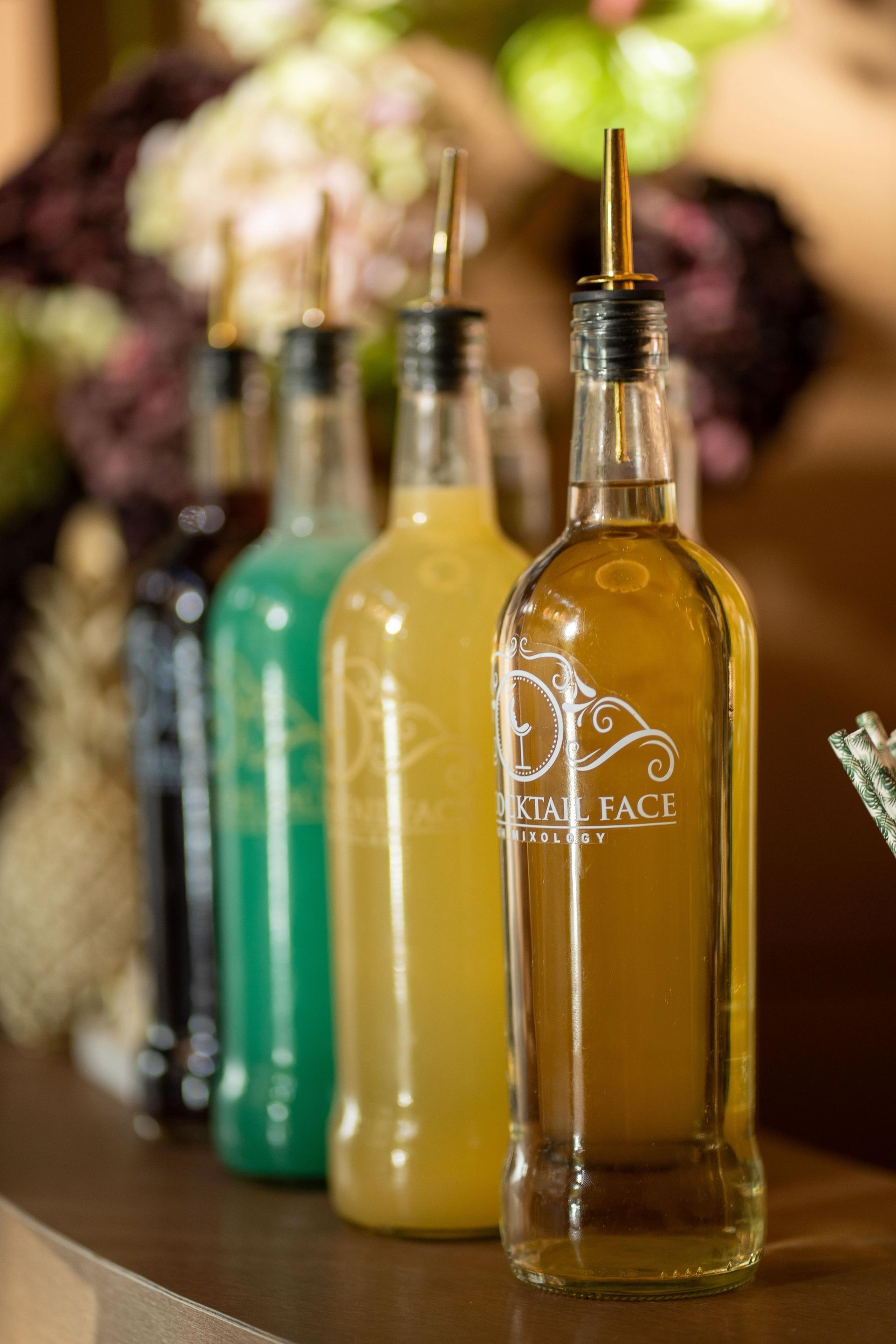 Botellas de coloridos mezcladores de cóctel con vertedores, alineadas en una barra.