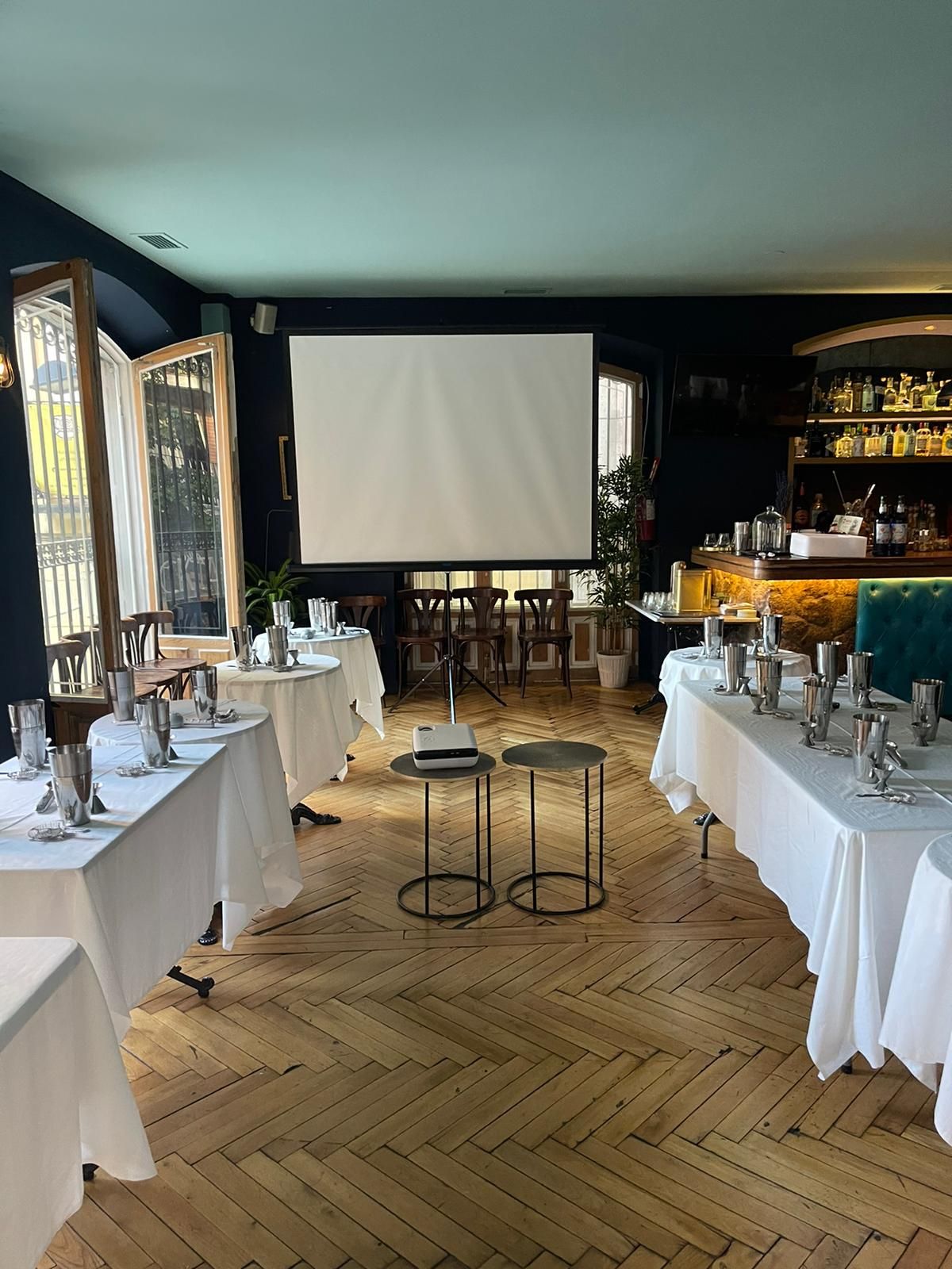 Montaje de restaurante para evento, con mesas con cubiertos, proyector y pantalla.