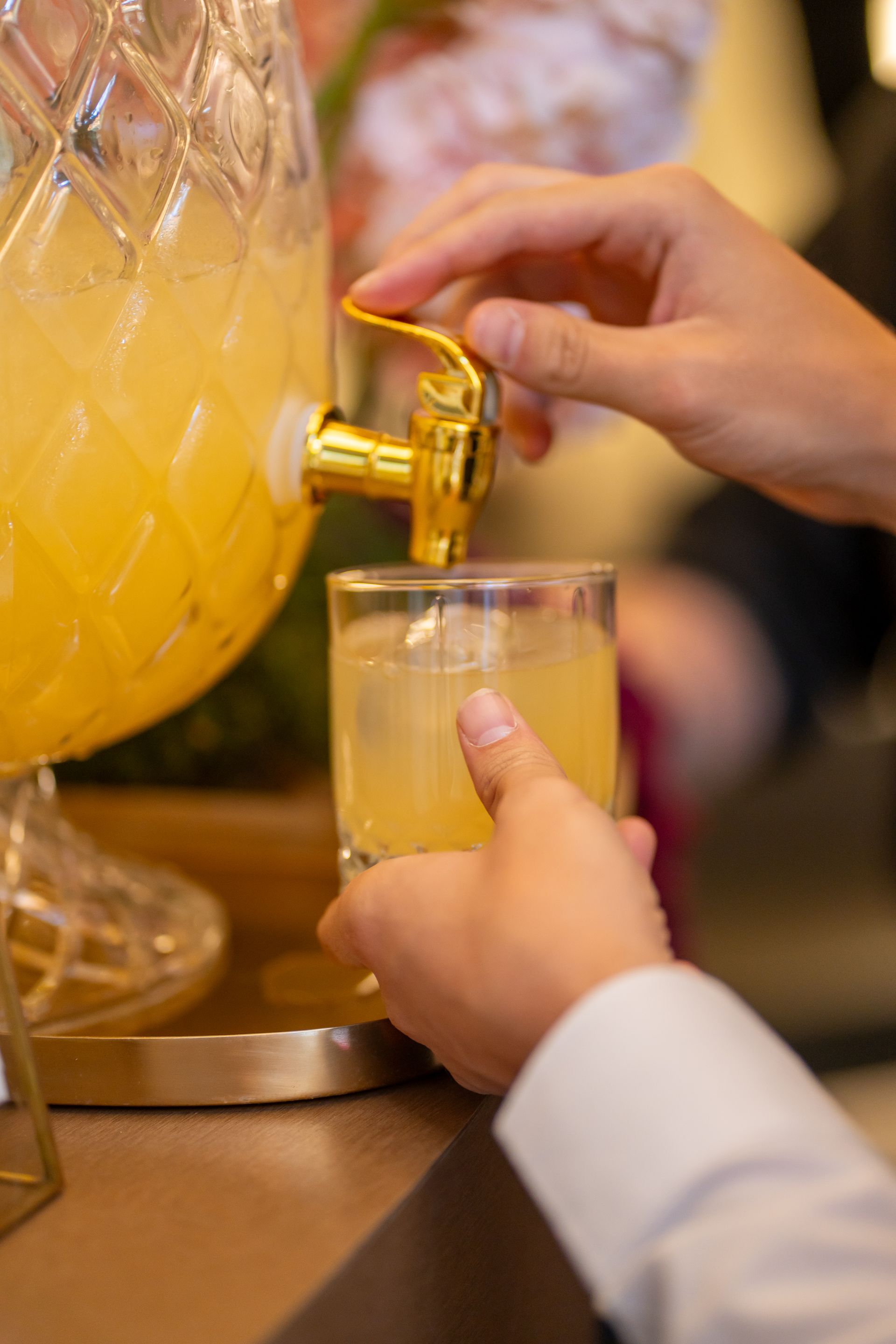 Persona vertiendo líquido amarillo de un grifo dorado en un vaso con hielo.