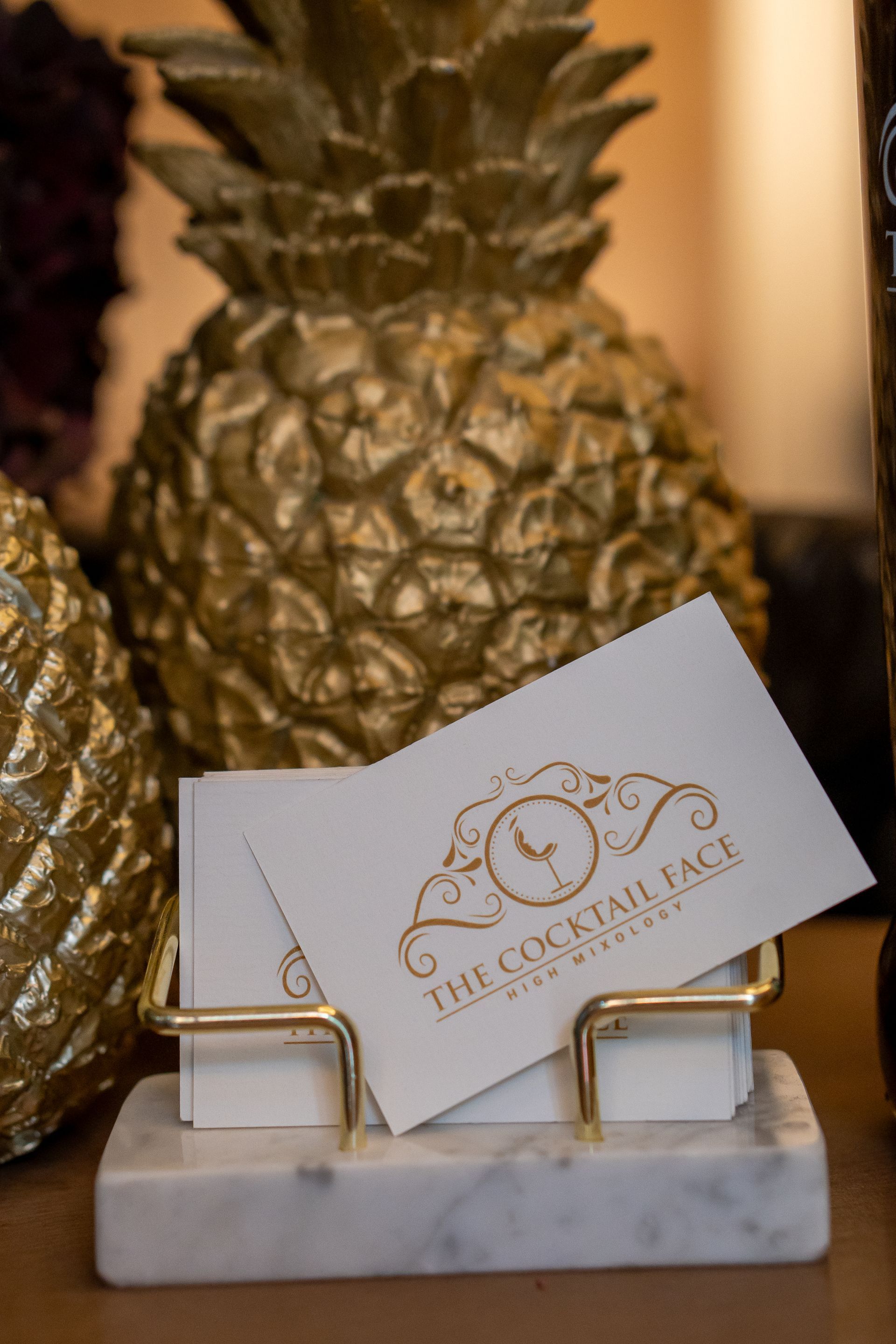 Tarjetas de visita en un tarjetero dorado con una piña dorada de fondo.