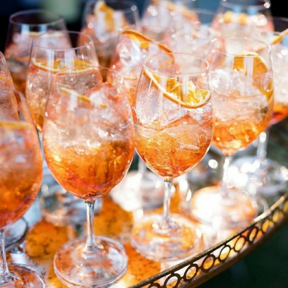 Camarero con chaleco blanco sirviendo de una botella detrás de la barra; cristalería y aperitivos delante.