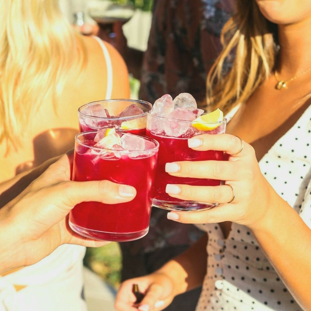 Tres personas brindando con cócteles rojos adornados con hielo y limón.