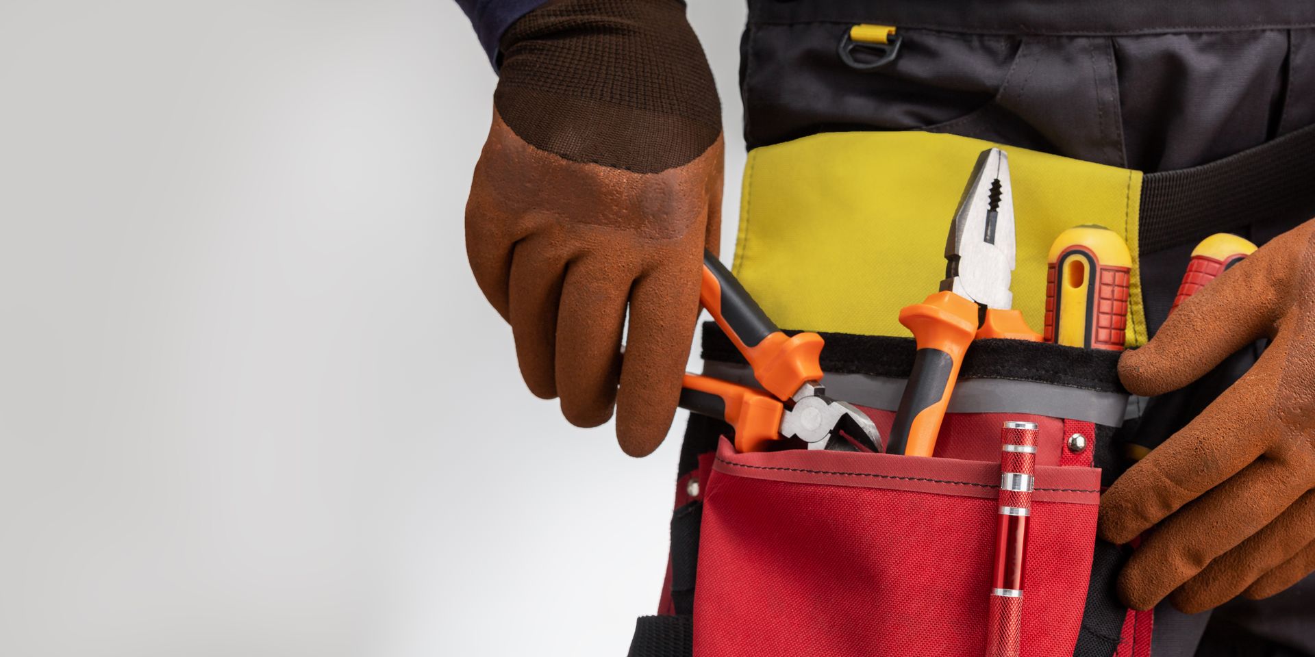 Une personne portant des gants de travail et une ceinture à outils contenant des pinces et des tournevis.