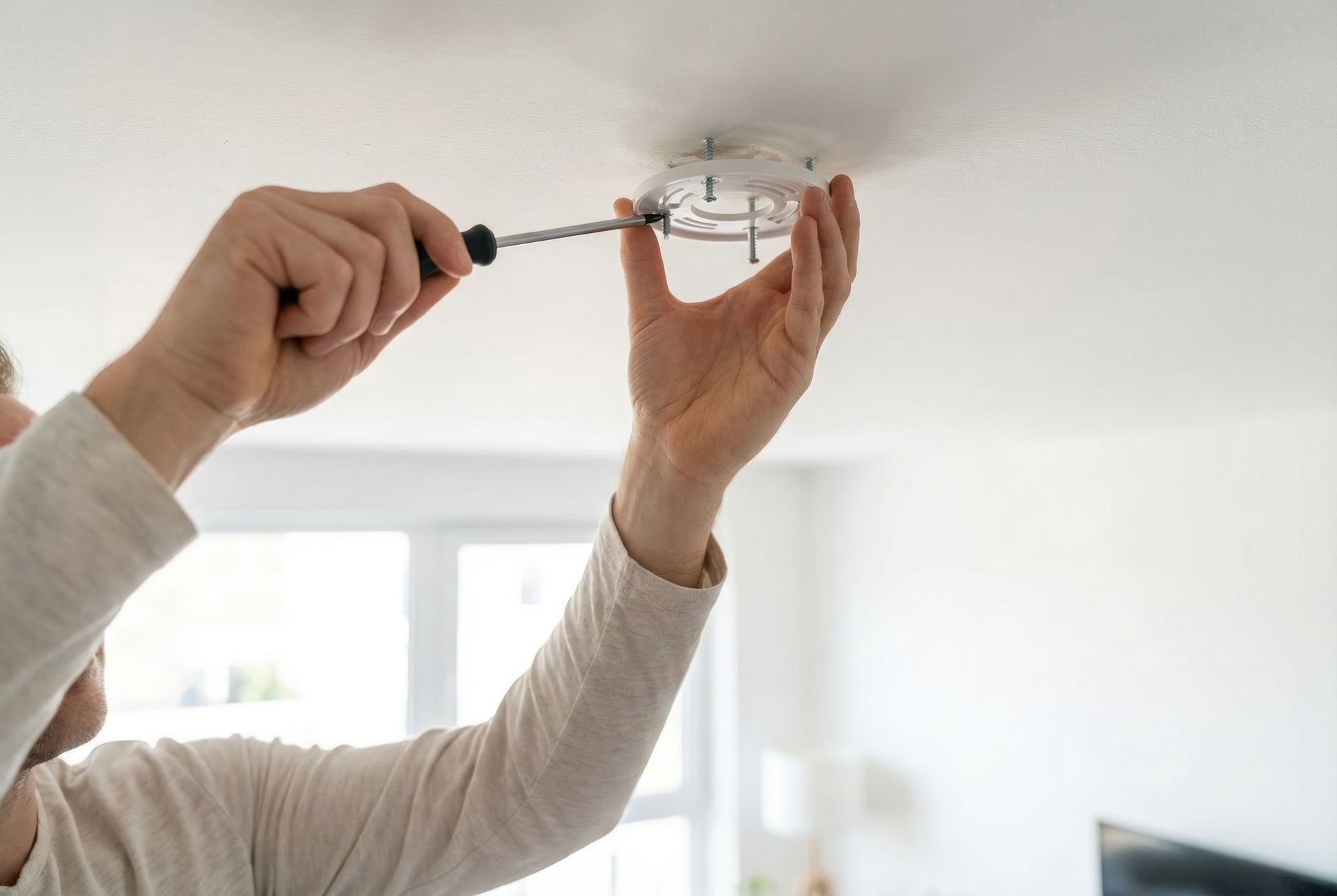 Une personne maintenant un support de fixation circulaire contre un plafond tout en serrant une vis avec un tournevis.