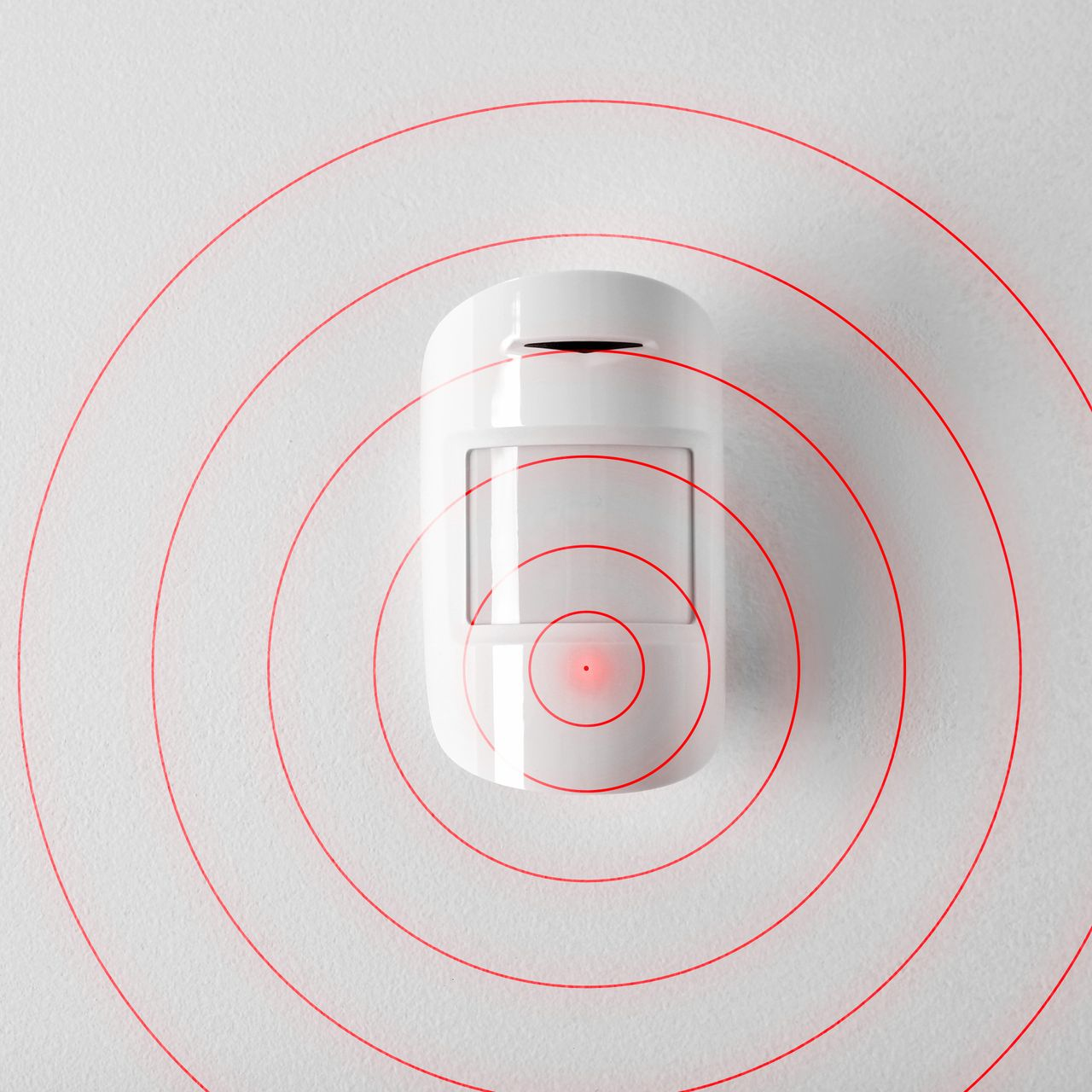 Un détecteur de mouvement blanc fixé au mur, des cercles concentriques rouges en émanent et représentent une zone de détection.