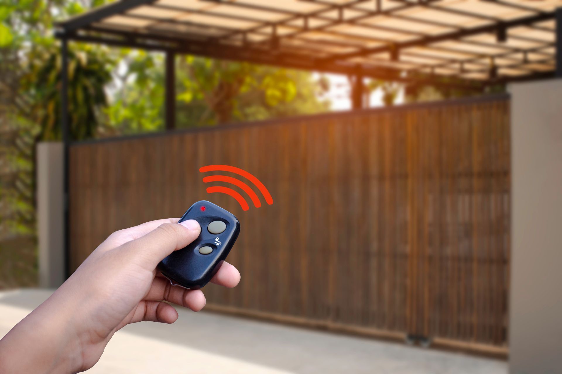 Une main tient une télécommande, la pointant vers un portail en bois, des ondes rouges indiquant qu'elle actionne le portail.