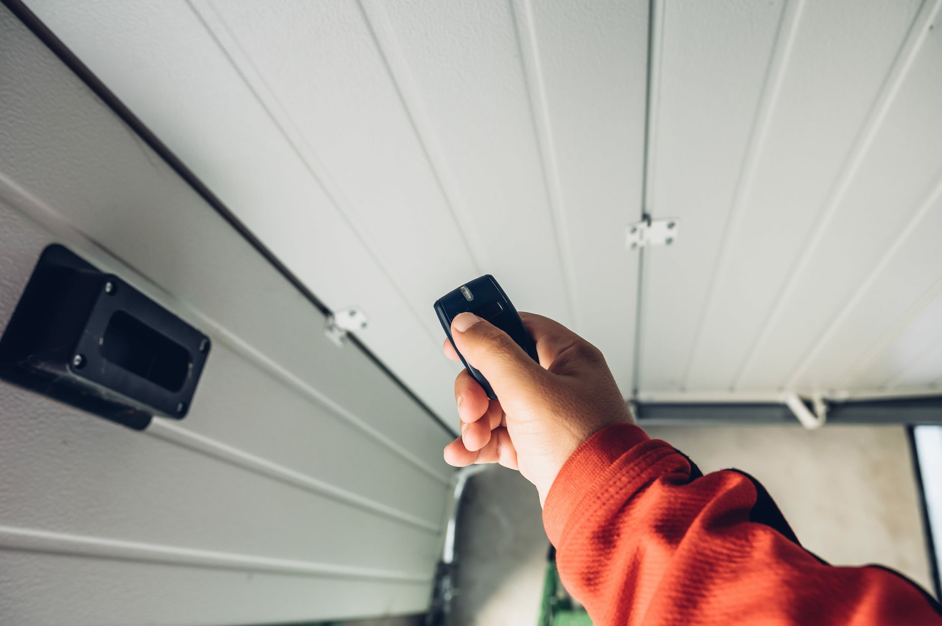 Une main pointe une télécommande vers une porte de garage blanche fermée.