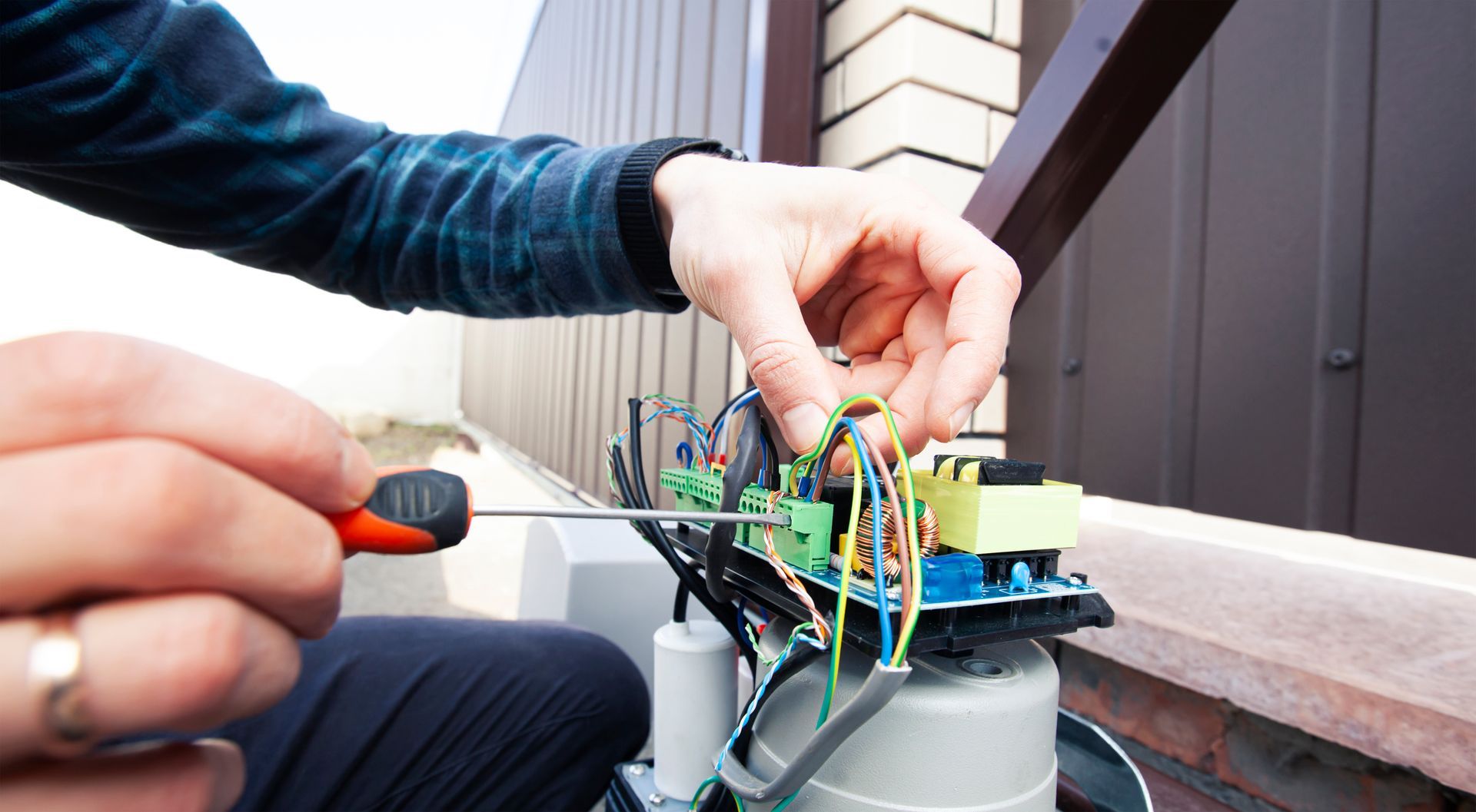 Des mains utilisent un tournevis pour connecter des fils à un bornier vert sur une carte de circuit imprimé électronique.