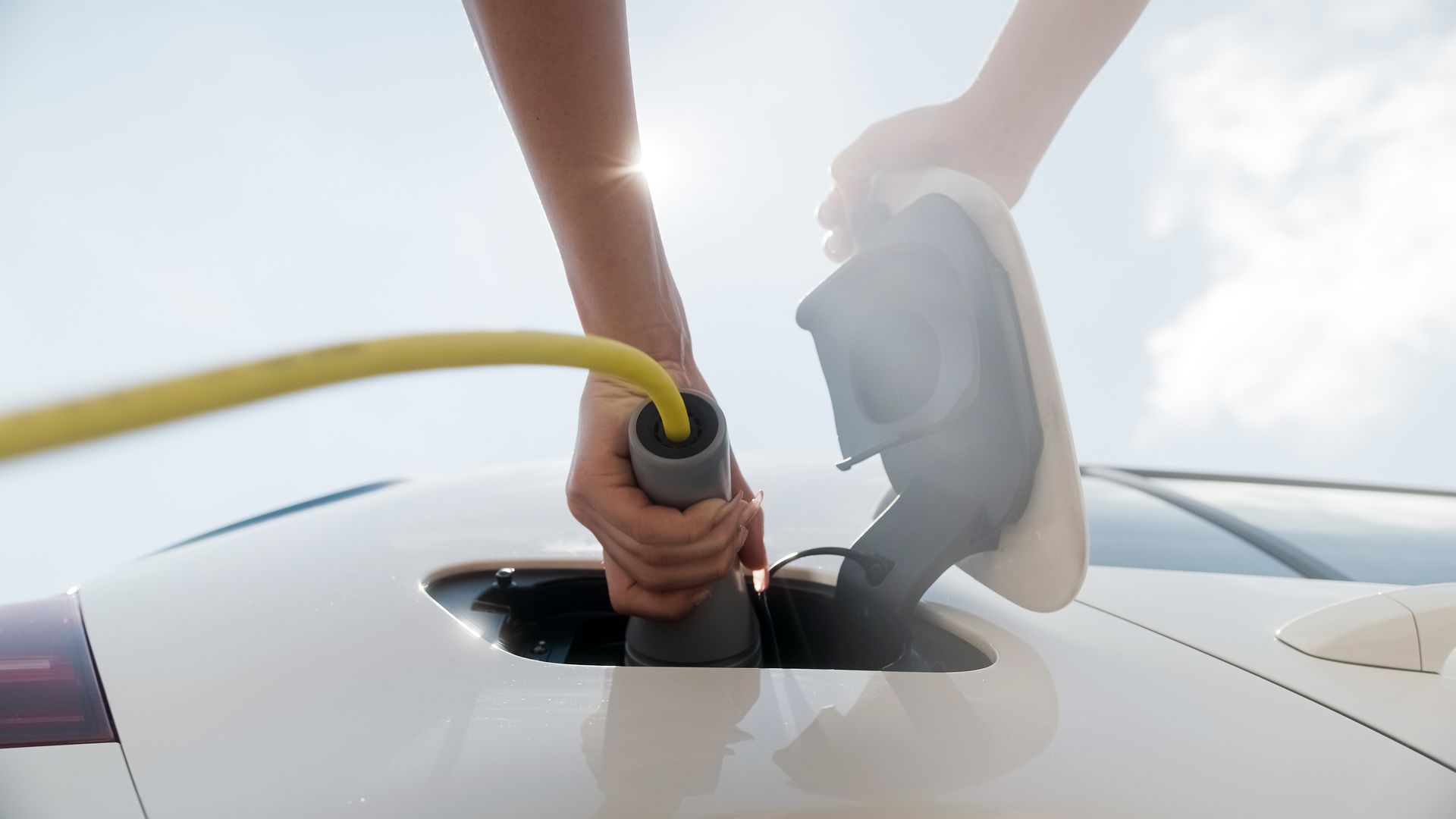 Les mains d'une personne branchant un câble de recharge jaune dans le port d'un véhicule électrique blanc.