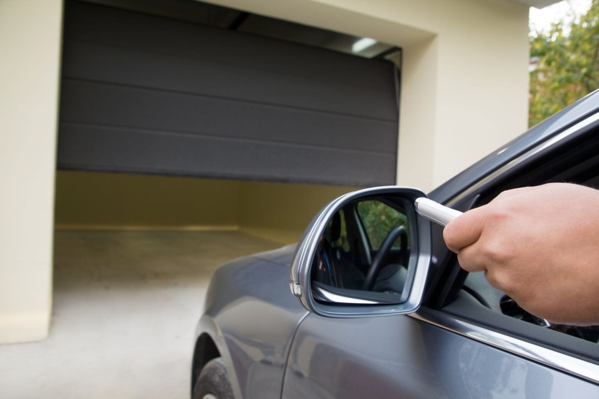 Une personne à bord d'une voiture grise utilise une télécommande pour ouvrir une porte de garage.